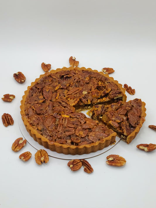A luxury gourmet pecan tart with a slice removed, surrounded by loose pecans on a clean white background by Let's Bake Cake Abu Dhabi
