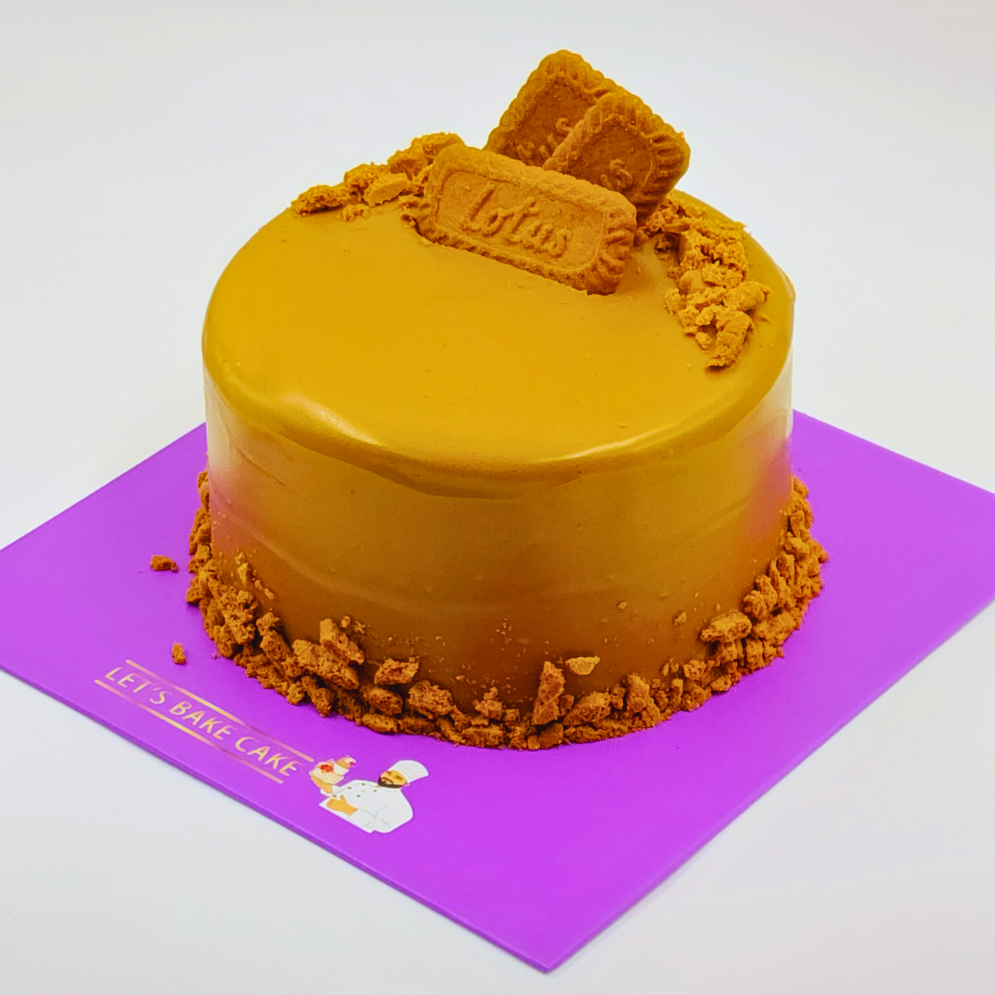 A luxury Lotus Biscoff cookie butter cake with a smooth caramel glaze and biscuit crumbles on a purple Let's Bake Cake board.
