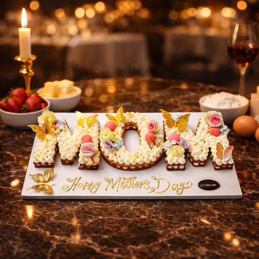 A luxury Mother's Day letter cake spelling 'MOM', decorated with gold butterflies, pink roses, and cream swirls on a marble table with candlelight, by Let's Bake Cake Abu Dhabi.